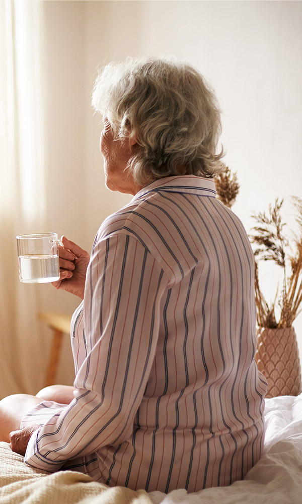 kobieta w piżamie siedząca na łóżku z kubkiem wody